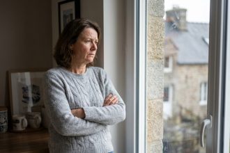 Femme d'âge moyen regardant par la fenêtre de sa cuisine bretonne